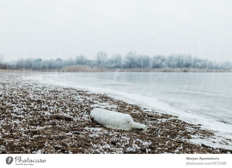 Glass bottle by the river in winter morning abandoned blue close-up coast cold country day decay dirt dirty dissolving dump ecology environment europe foggy