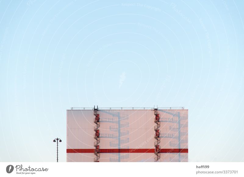 double red spiral staircase in front of a white façade with long shadows in the early morning and a lantern on the side with a light blue, cloudless sky Sunrise