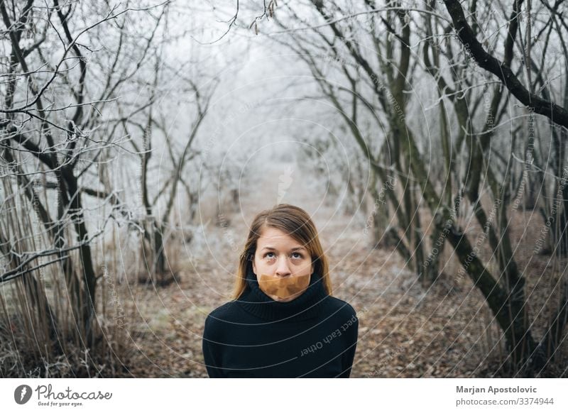 Woman with tape on her mouth in cold winter forest adult anxiety behavior blond caucasian censorship civil concepts depression despair distraught emotional