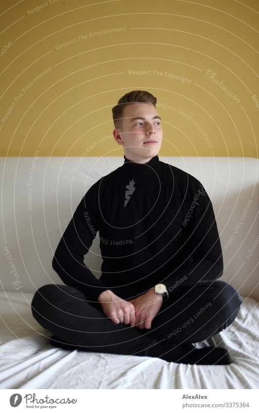 Young man sitting cross-legged on bed in front of yellow wall Lifestyle Style Joy Beautiful Well-being Bed Room Bedroom Youth (Young adults) 18 - 30 years