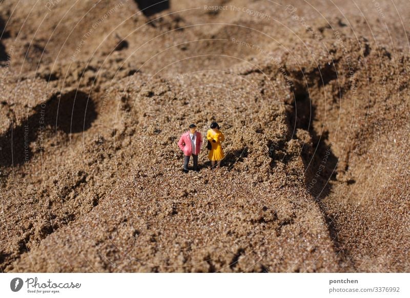 Two model figures - male and female - in the sand on the beach Couple Man Woman Beach Sand get stuck Humor bizarre Small Manikin Toys vacation Summer