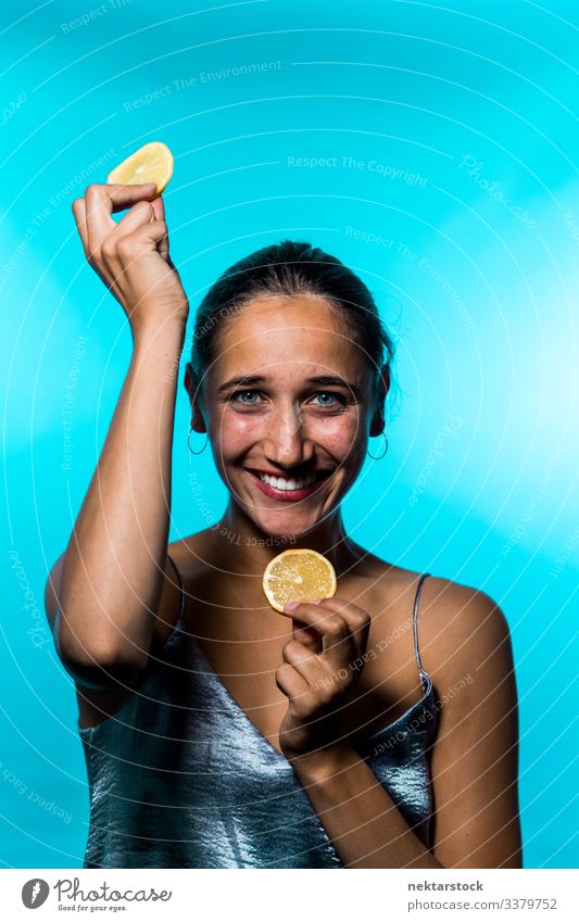 Young Woman Holding Up Lemon Slices on Blue Background lemon slice female girl holding up concept minimalism citrus fruit fresh freshness smile happiness