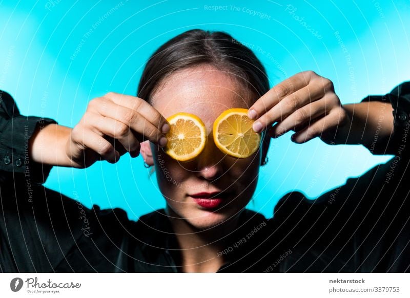 Caucasian Woman Covering Eyes with Lemon Slices on Blue Background lemon slice covering female girl eyes holding up concept minimalism citrus fruit fresh