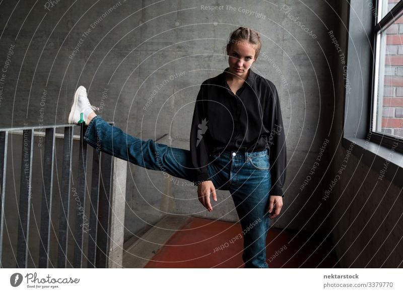 Young Woman with Leg on Staircase Handrail Looking at Camera leg handrail leg raised female girl woman stretch young adult youth culture day female beauty