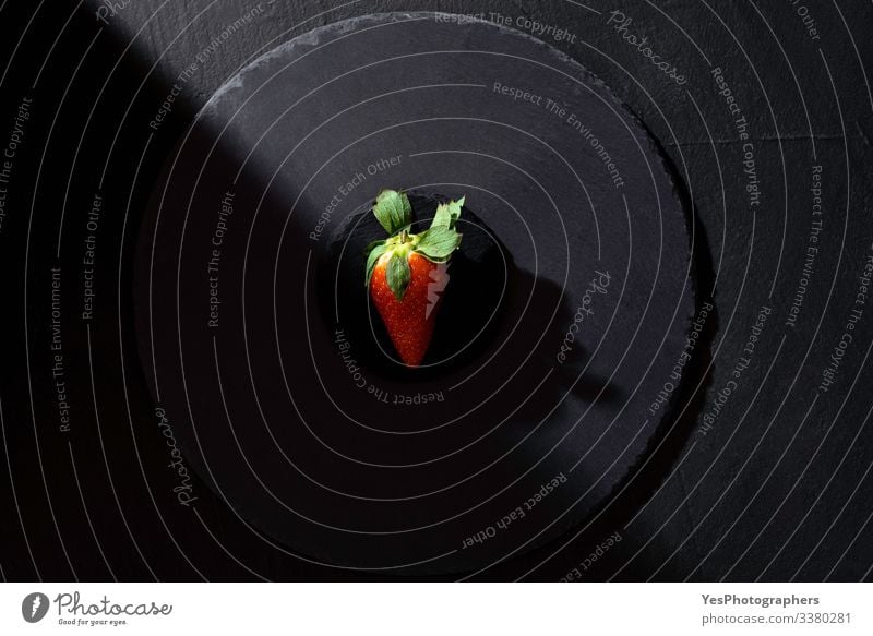 Single strawberry on black platter in harsh light. Fruit Dessert Organic produce Healthy Eating Fresh above view all black black background diet food flat lay