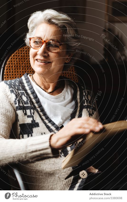 Elderly woman reading by window with enthusiasm book elderly knowledge literature concentrate information intelligent smart creative glasses relax hobby