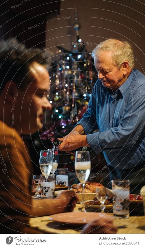 Old man pouring champagne in glasses during Christmas dinner at home christmas celebrate bottle aged senior casual drink beverage male alcohol lifestyle