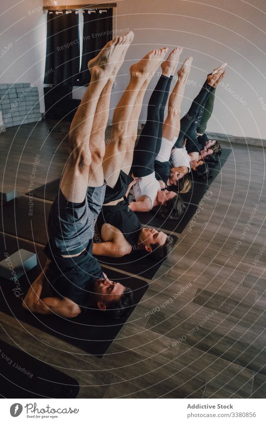 Focused athletes practicing yoga together performing supported shoulderstand balance position in contemporary gym gymnastic stretch exercise training leg