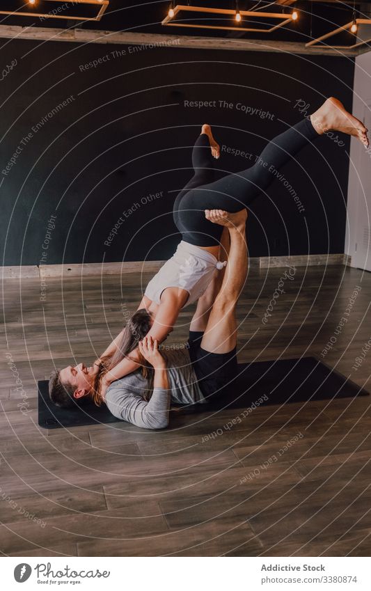 Cheerful couple training together standing in folded leaf position on mat together in studio acro yoga folded leaf pose balance partner cheerful athletic