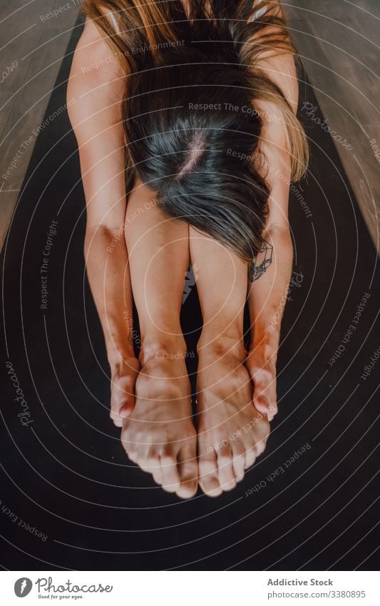 Diligent woman practicing yoga in seated forward bend position while having class in contemporary studio practice pose flexible body stretch barefoot gymnastic