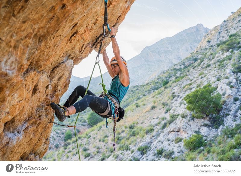 Concentrated young female climber ascending on cliff in summer woman alpinist mountain practice climbing active mountaineering risk travel brave adventure