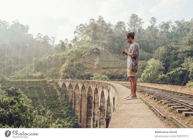 Man on vacation browsing smartphone on bridge man tourism travel watching take photo landscape tropical using mobile phone sri lanka asia green plant exotic