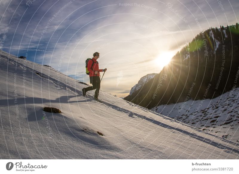 Woman with hiking backpack and walking sticks in the mountains, snow-covered landscape in winter. Snow Sunset Alps Berchtesgaden Alpes Tracks Winter hike