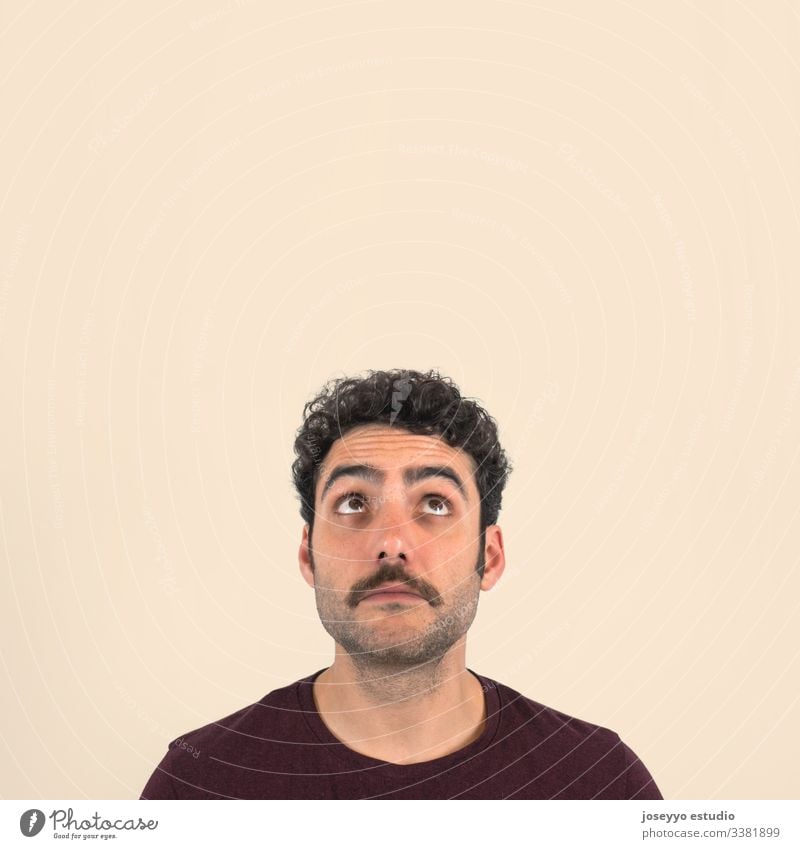 Funny portrait of a young boy with a mustache with doubtful and bewilderment  face  looking up. Purple t-shirt and isolated ochre background. 30-40 years