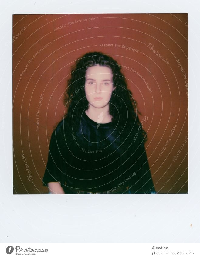 Analog Polaroid portrait of a young woman in front of a red wall Looking into the camera Central perspective Shallow depth of field Artificial light Day