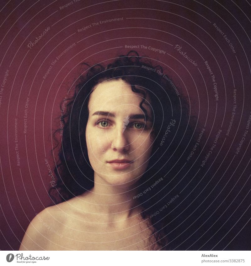 Analogue portrait of a young woman in front of a red wall Looking into the camera Central perspective Shallow depth of field Artificial light Day