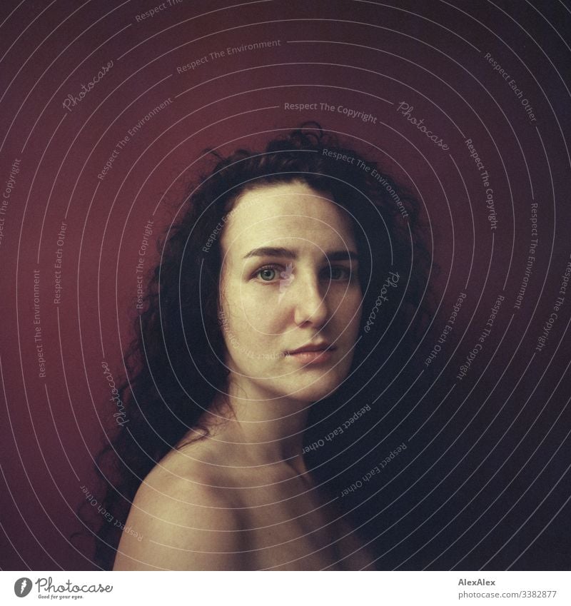 Analogue portrait of a young woman in front of a red wall Looking into the camera Central perspective Shallow depth of field Artificial light Day