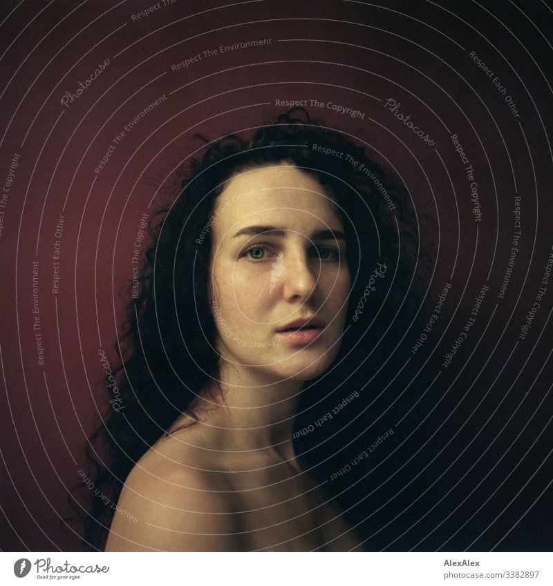 Analogue portrait of a young woman in front of a red wall Looking into the camera Central perspective Shallow depth of field Artificial light Day