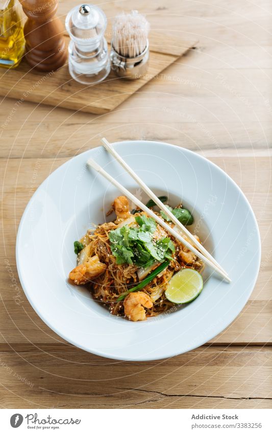 Asian dish of noodles with shrimps in restaurant chopsticks asian food haute cuisine lime greenery herb parsley seafood plate wooden organic tasty table fresh