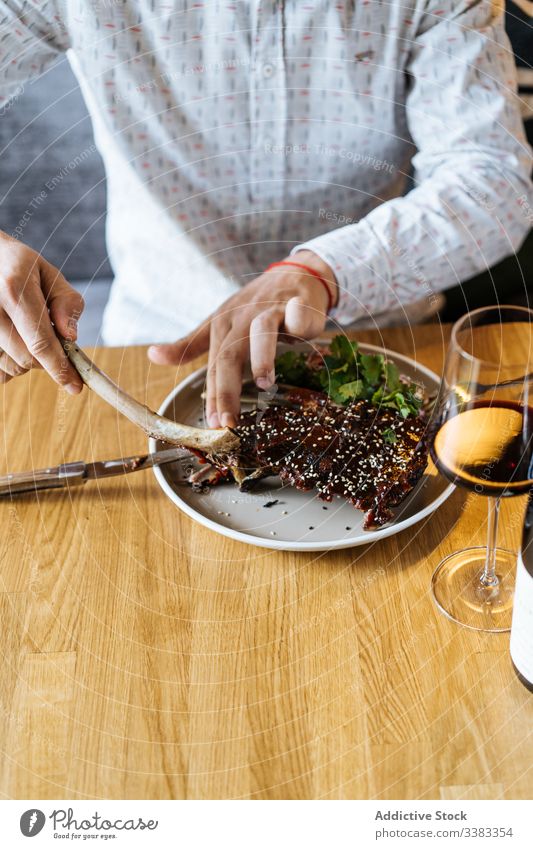 Person eating beef ribs served at table with wine in restaurant green knife fork glazed person drink gourmet delicious dinner fresh tasty gastronomy lunch sauce