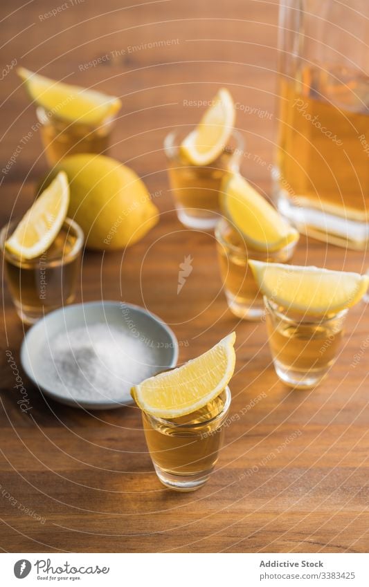 Tequila in shots with salt rim and lemon alcohol tequila booze table wooden glass beverage drink fresh tasty citrus orange party delicious yellow organic food