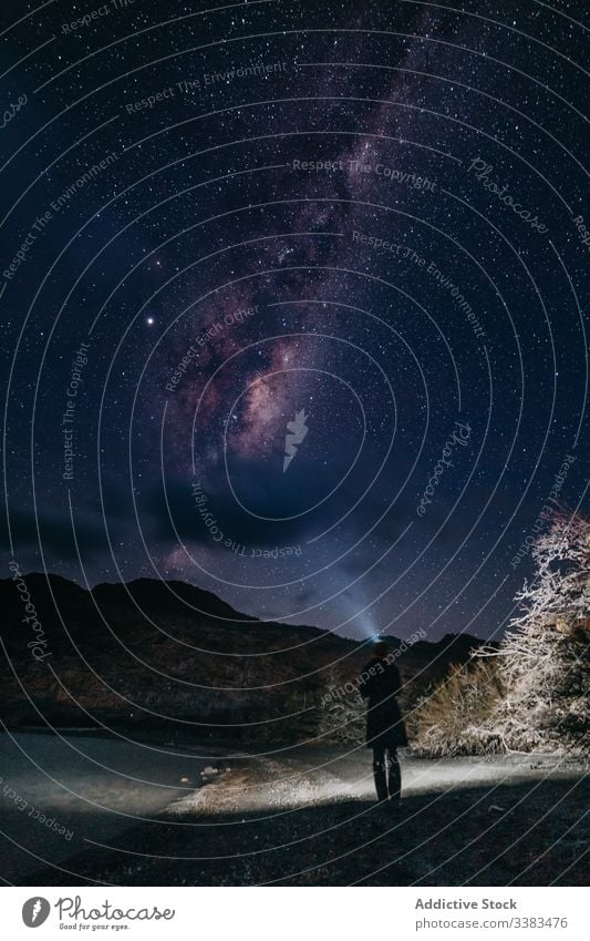 Traveler on beach of frozen pond in highland under majestic night sky with Milky Way travel milky way hill starry silhouette coast person water tranquil