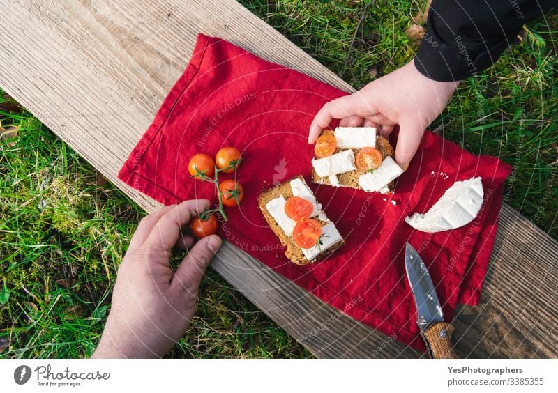 Serving food outdoor on grass. Picnic in sunlight on wood plank above view bread break camping cheese eating outdoor garden gourmet grabbing green grass hands