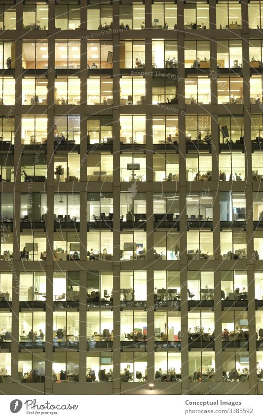 Exterior of an office at dusk, revealing the daily activity of the workers office block exterior overworked business people ambition architecture