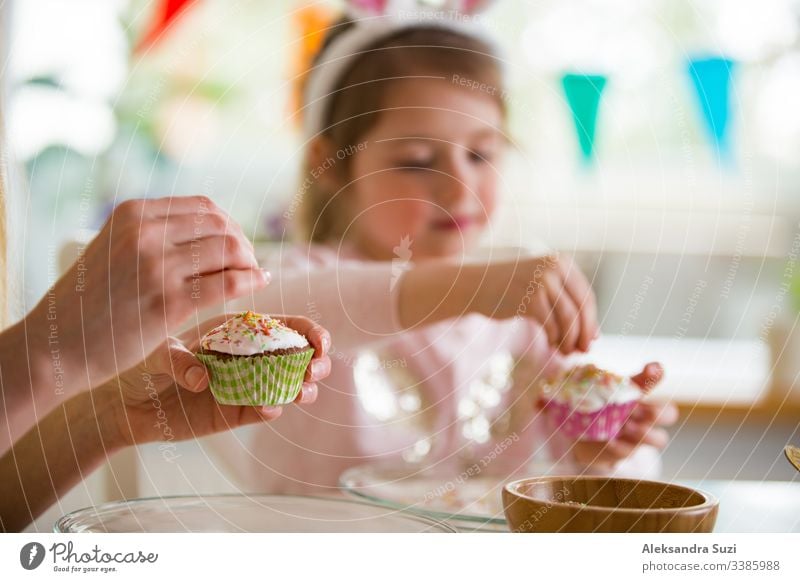 Mother and daughter celebrating Easter, cooking cupcakes, covering with glaze. Happy family holiday. Cute little girl in bunny ears. baking candid celebration