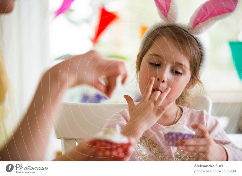 Mother and daughter celebrating Easter, cooking cupcakes, covering with glaze. Happy family holiday. Cute little girl in bunny ears. baking candid celebration