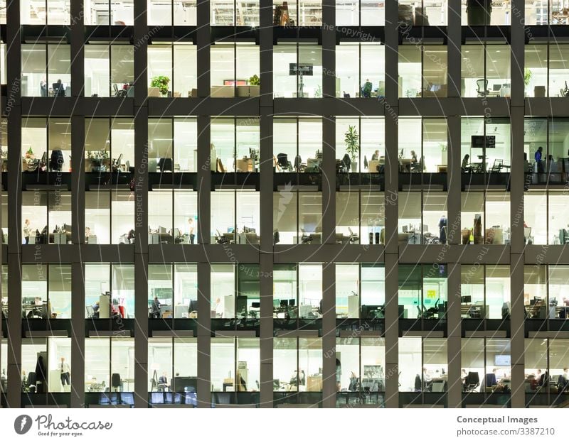 Modern office building at dusk, revealing the daily activity of the workers office block exterior overworked business people ambition architecture