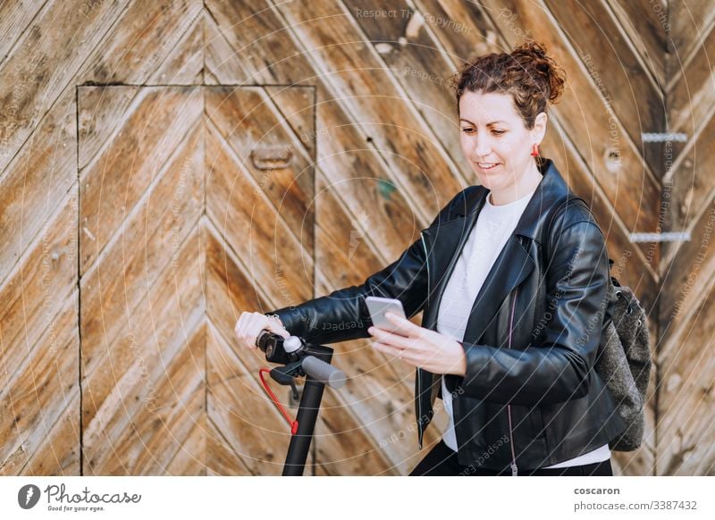 Middle aged woman riding his electric scooter and looking at mobile phone. active activity app autumn background beautiful bike blond booking cars city