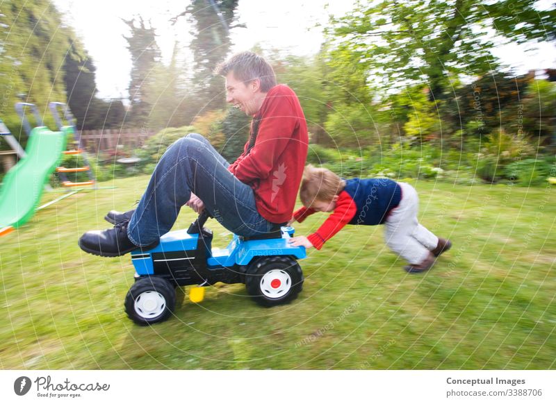 A young boy pushing a man on a toy tractor action adventure blurred motion bonding carefree caucasian cheerful child childhood cooperation determination driving