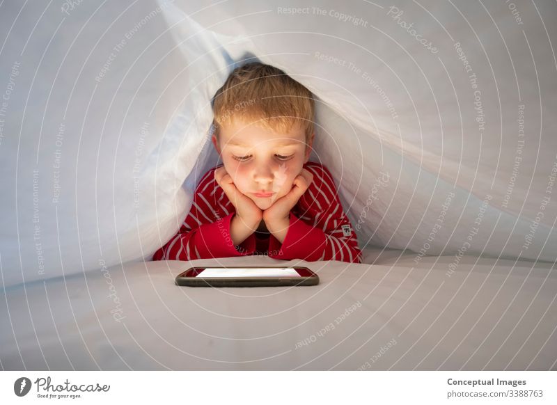 Caucasian boy in his bed using smartphone to make video call to talk to friend childhood facetime mobile touch technology digital finger smiling lifestyle fun