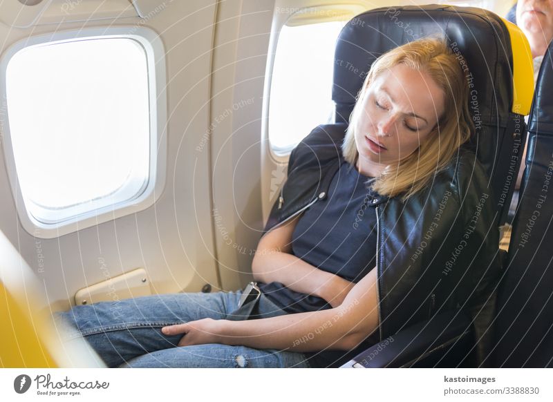 Tired blonde casual caucasian lady napping on seat while traveling by airplane. sleep woman flight business economy stress trip airline window space confortable