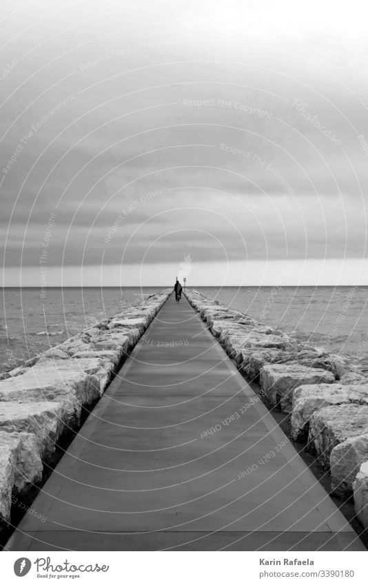 Cyclists in black and white Gloomy Gray Dreary Cold Exterior shot Ocean stones Waves Bicycle Loneliness Water Bad weather Coast