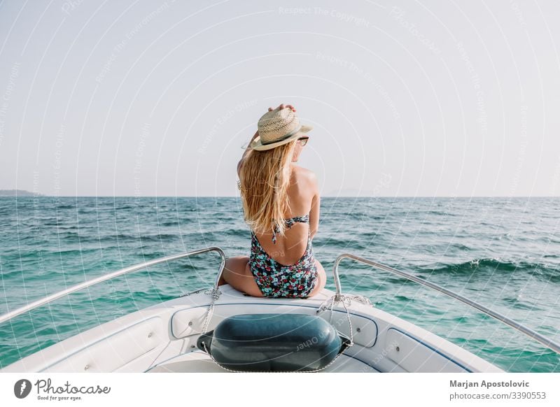 Young woman enjoying on deck of a boat on the sea young ocean water cruise leisure relaxing vacation summer holiday travel tourism sunbathing bow hat blonde