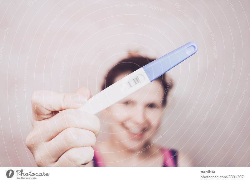 Young happy woman holding a positive pregnancy test pregnant mom mother family happiness mood emotion emotive optimism femininity feminine pink growth life