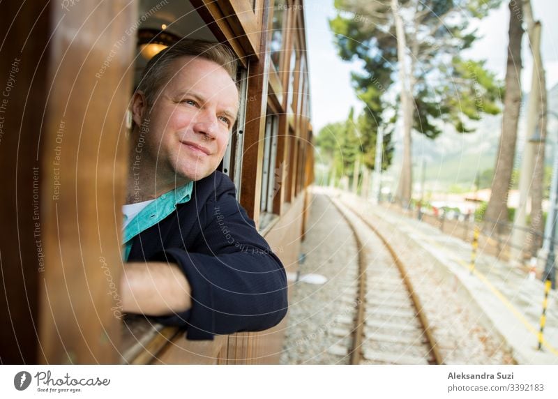 Man traveling by retro wooden train, looking through the window. Beautiful landscape of mountains. Majorca, Spain. adventure alone beautiful blond cheerful