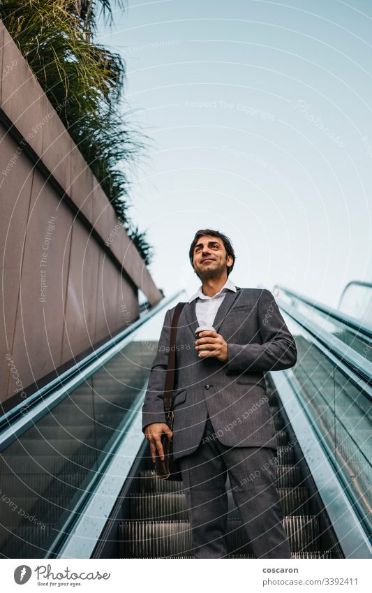 Businessman in a suit drinking a coffee and riding up an escalator adult airport attractive boss business business people business wear businessman