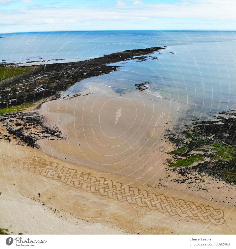 Giant sand art Celtic knot work braid along a beach with a person for scale created by dji camera Celtic design coast sustainable ecotourism environment nature