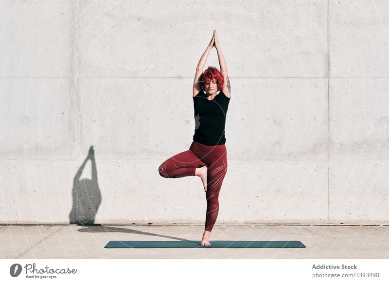 Woman doing balance exercise in tree pose while practicing yoga on street athlete namaste woman meditate practice training stretch barefoot concrete calm