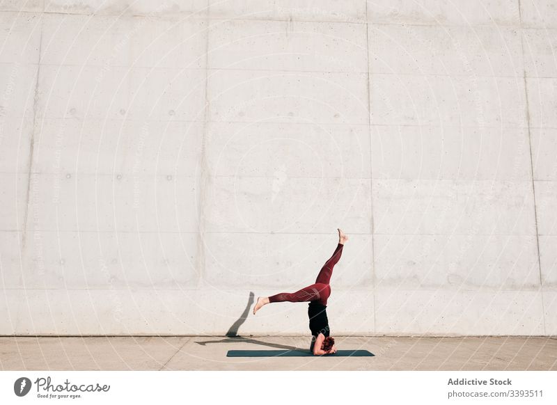 Woman doing balance exercise in headstand with split pose while practicing yoga on street woman acrobatic practice training urban sirsasana concrete strong