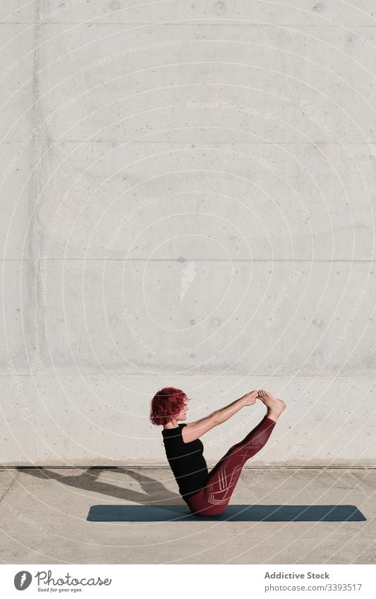 Flexible young sportswoman practicing yoga in balance paripurna navasana on street boat pose flexible exercise stretch acrobatic practice training gymnastic