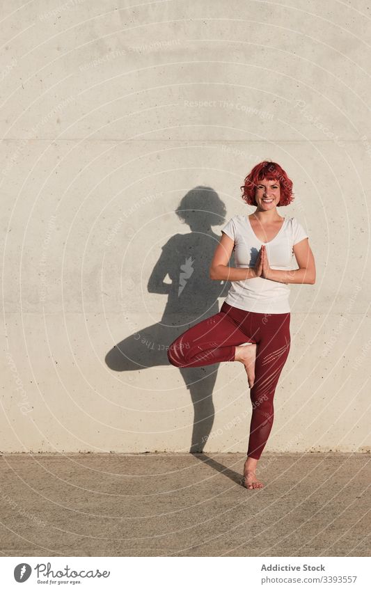 Woman doing balance exercise in tree pose while practicing yoga on street athlete namaste woman meditate practice training stretch barefoot concrete calm