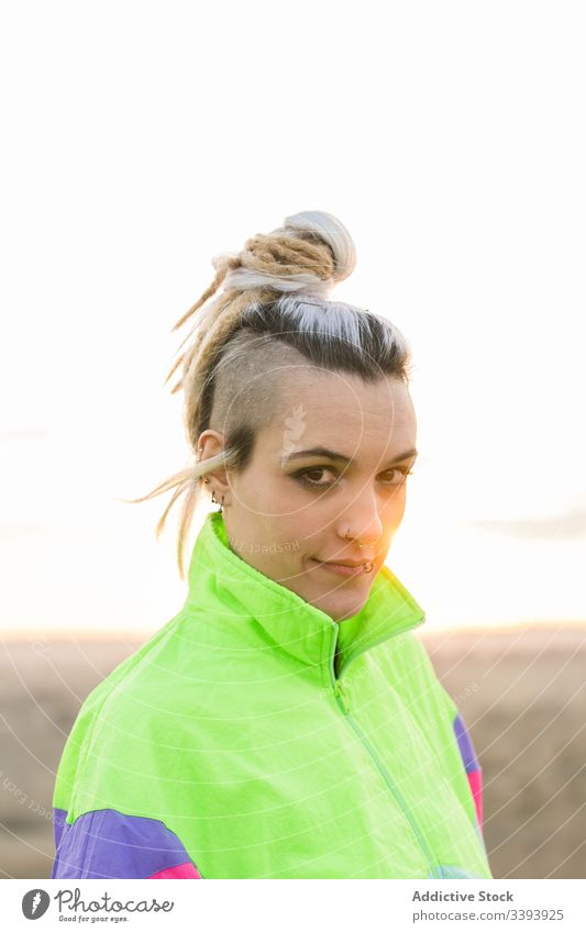 Young woman with modern hairstyle in colorful sportswear teenage hipster extraordinary pensive cool nature jacket dyed hair contemporary female sky sunset