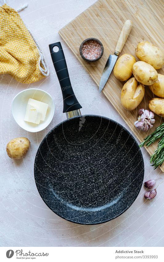 Cooking ingredients near frying pan cook kitchen napkin cutting board knife seasoning potato food preparation fresh ripe spice herb rosemary salt butter dish