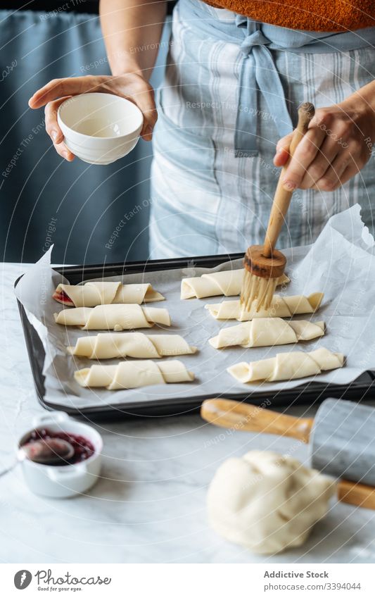 Cook holding bowl and brushing croissants in baking sheet on table cook jam dough preparation sliced bakery homemade culinary making sweet raw dessert recipe