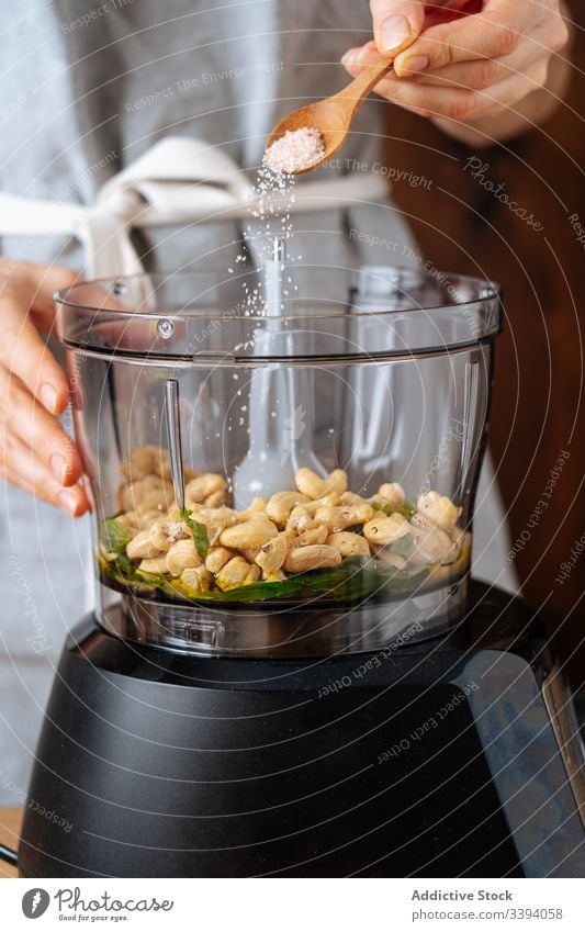 Crop lady adding salt into blender woman cook spill juicer cashew kitchen vegan healthy dish kitchenware appliance food preparation home meal diet ingredient