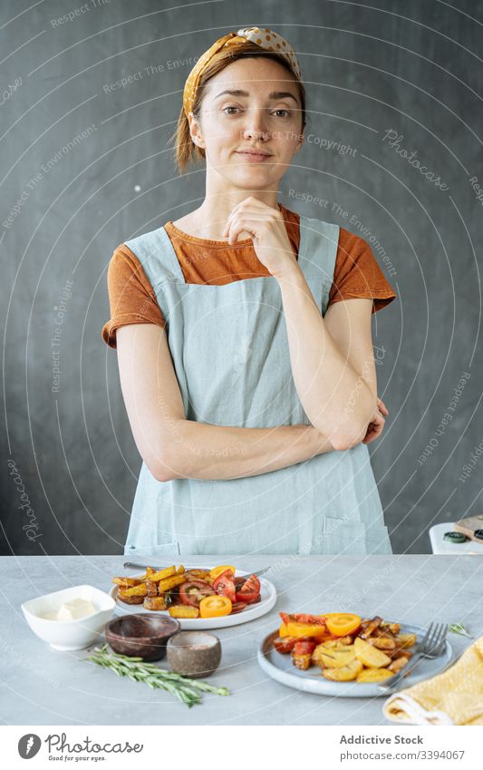 Confident woman standing near table with roasted vegetables cook kitchen dish fried lunch plate food preparation female home meal ingredient baked tasty